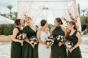 Bridesmaids in elegant black dresses pose with pink and white floral bouquets at an outdoor wedding venue.