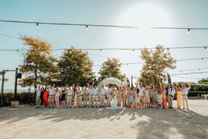 Wedding party poses along a waterfront boardwalk with string lights overhead during golden hour sunset.