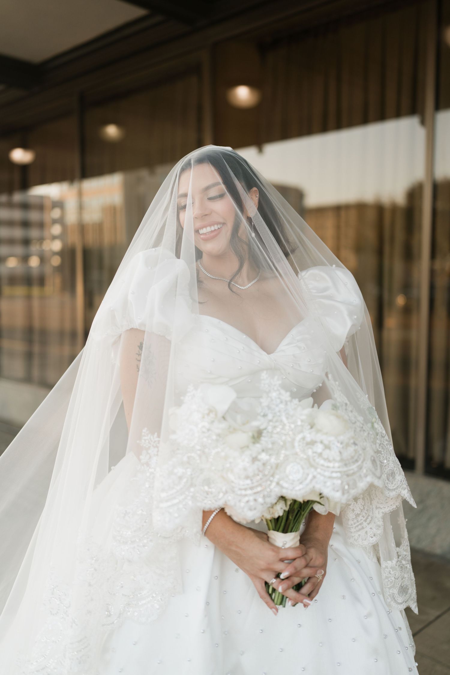 Romantic wedding couple in white attire dancing in light-filled reception venue with draped fabric decor.