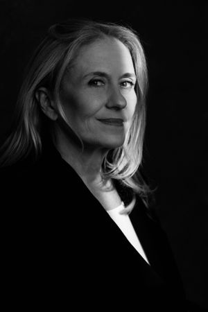 Dramatic black and white portrait of a mature woman in business attire against dark background.