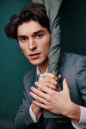 Artistic portrait of person in grey suit against teal background with fabric.