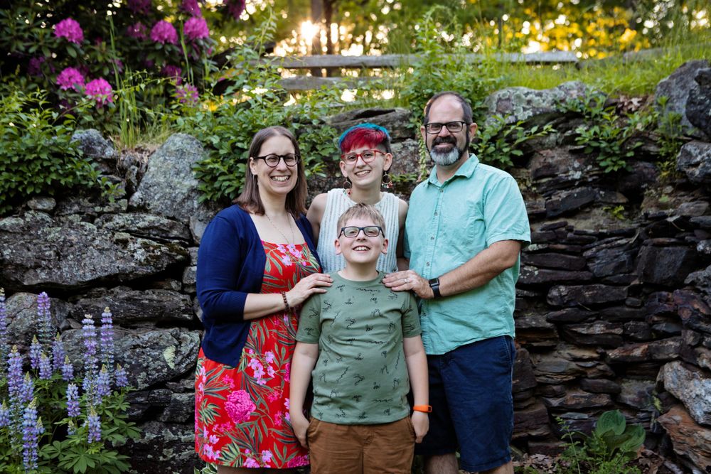 Family with two children smiling in front of stone wall and flower garden at sunset