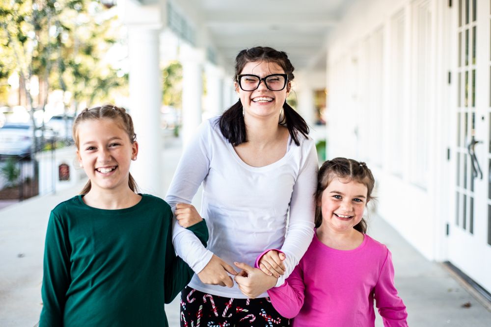 Three people in casual wear smile while standing together on a white porch.
