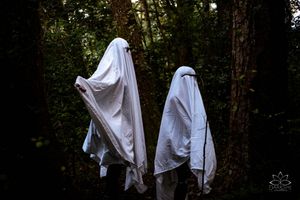 Two ghost-like figures in white sheets standing in a dark forest setting.