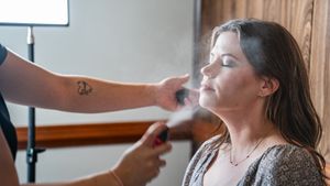 Makeup artist applying setting spray to a young woman's face in a professional studio setting.