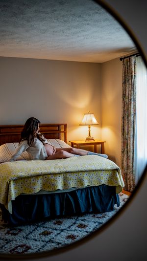 Woman sitting on a bed in a warmly lit hotel room, viewed through a round mirror reflection.