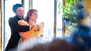 Bride and groom sharing a happy embrace at wedding reception near large windows with natural light.