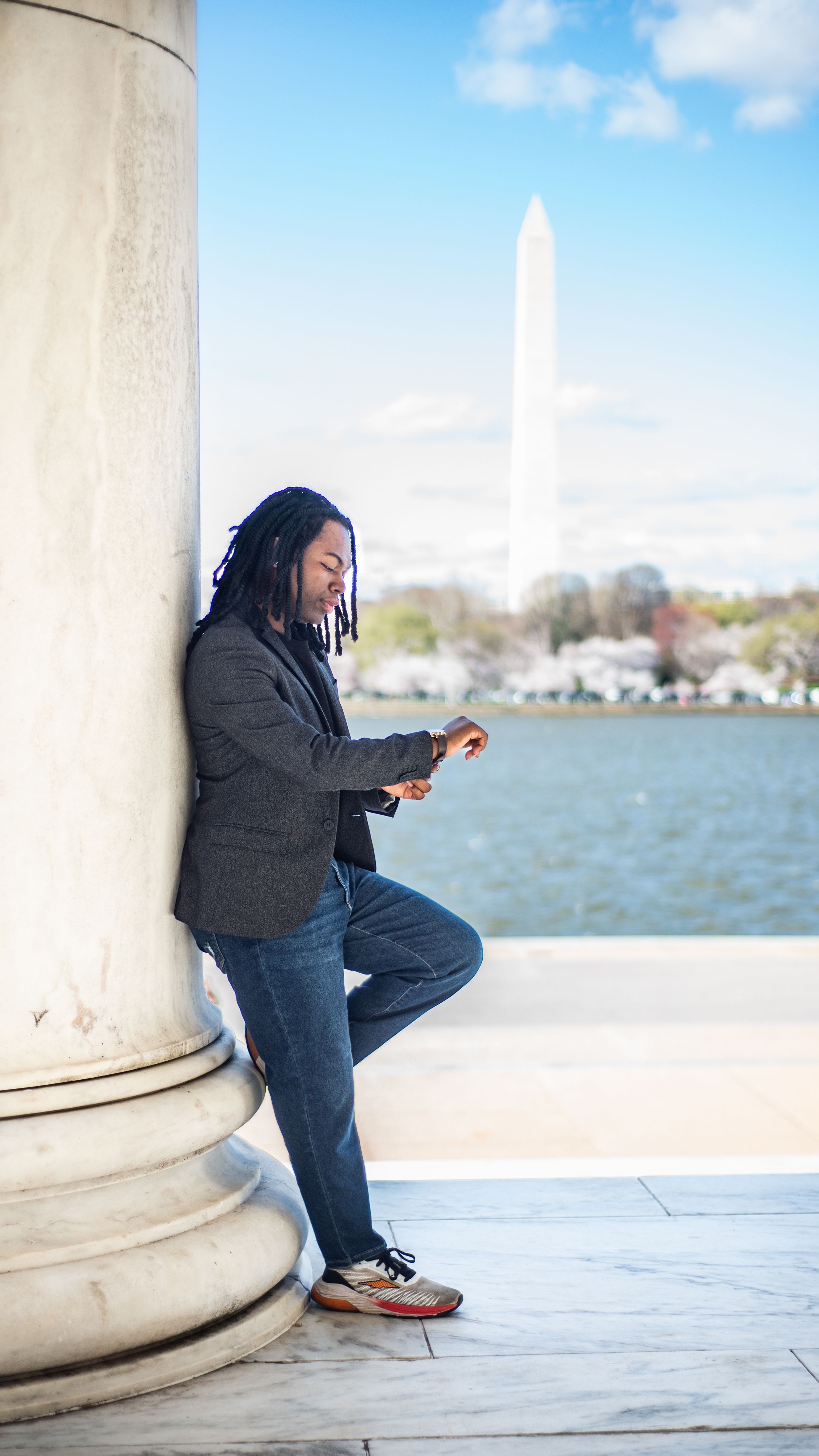 Man with dreadlocks leaning against a column at the Jefferson Memorial with the Washington Monument in the background.