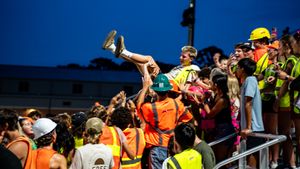 Excited crowd of spectators in colorful clothing cheers during an evening outdoor event.
