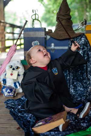 Baby in Harry Potter themed outfit laughs joyfully while surrounded by magical props and decorations on a porch.
