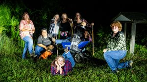 A group of people gather outdoors in a backyard setting at night with string lights creating a cozy atmosphere.
