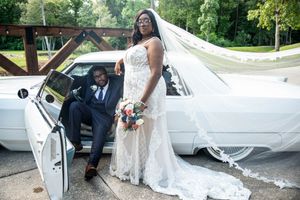 A couple posing with their classic white car during a wedding.