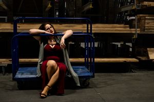 A person in a red dress lounges dramatically on a wooden bench in an industrial-style studio setting.