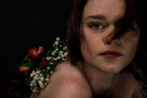 Artistic portrait shot with red and white flowers in dark moody lighting.