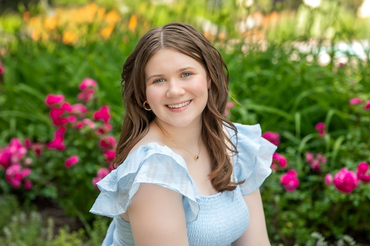 Portrait in garden setting with blooming pink flowers and greenery.