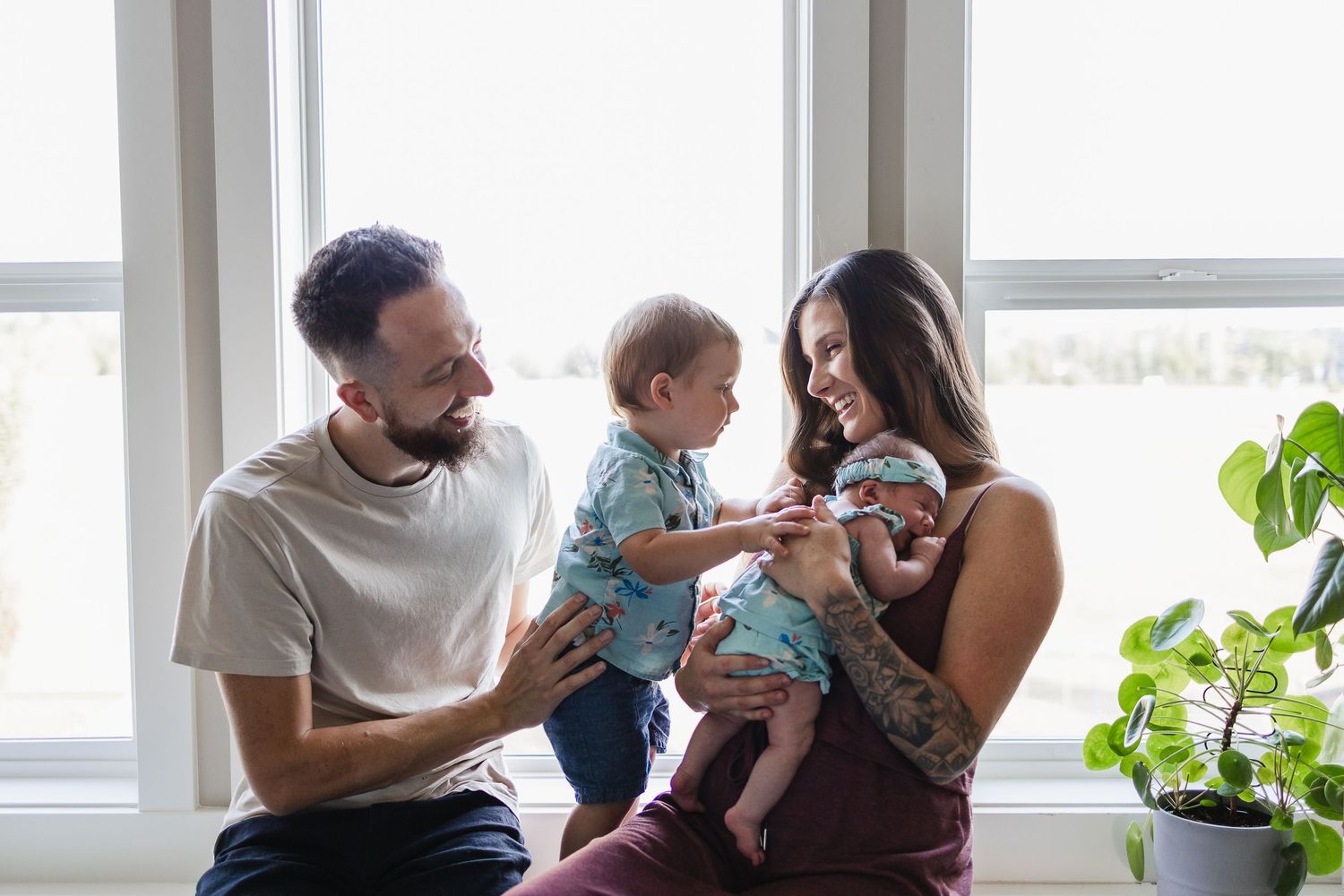 Parents and two young children sit on a window sill smiling together