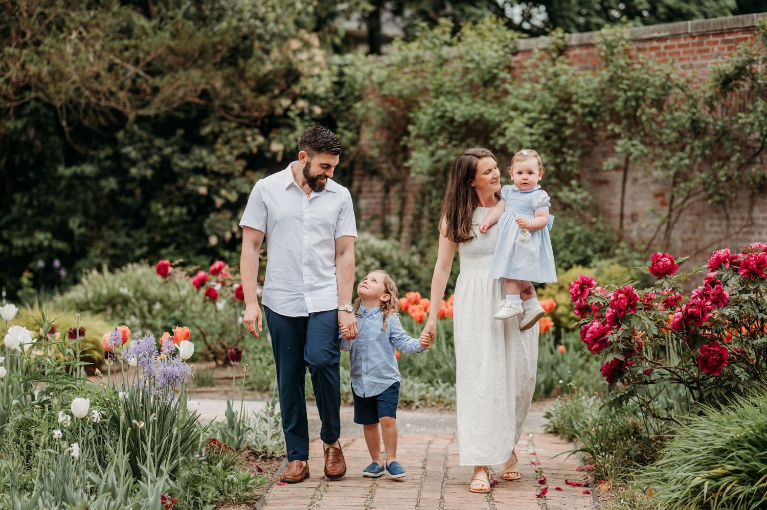 A family walks together along a garden path surrounded by vibrant flowers and greenery on a sunny day in Montclair.