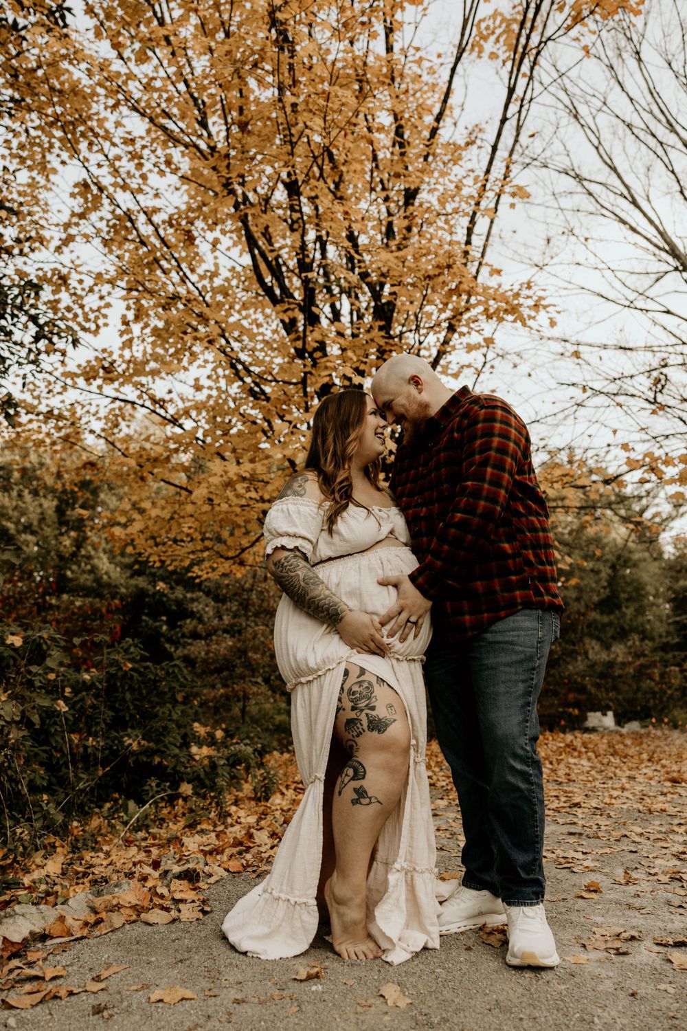 A couple shares an intimate autumn moment on a leaf-covered path surrounded by golden trees in warm sepia tones.