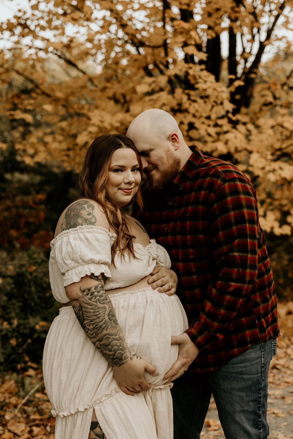 A couple embraces outdoors during fall season, with golden autumn leaves in background.
