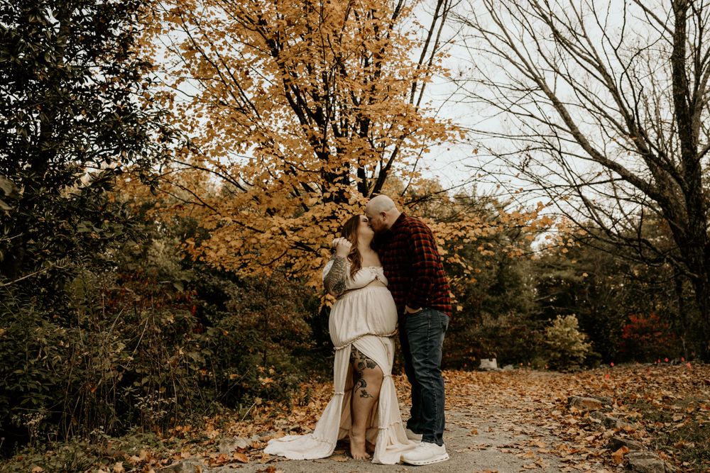 Couple sharing an intimate moment on a path surrounded by autumn trees with golden leaves.