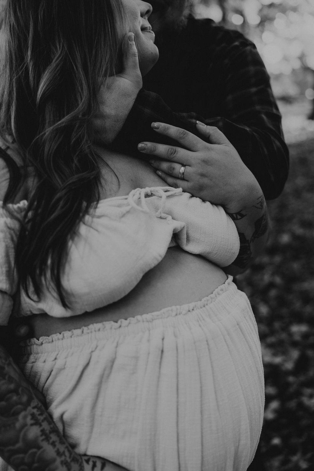 Black and white maternity photo showing hands tenderly embracing a pregnant belly in a flowy white dress.