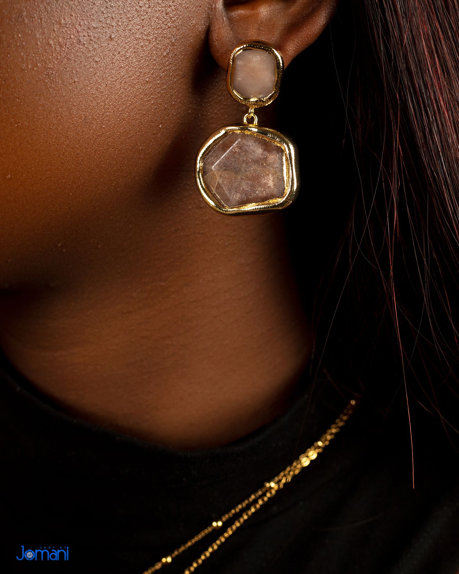 Faceted gemstone drop earrings in gold setting worn with black top and gold chain necklace.