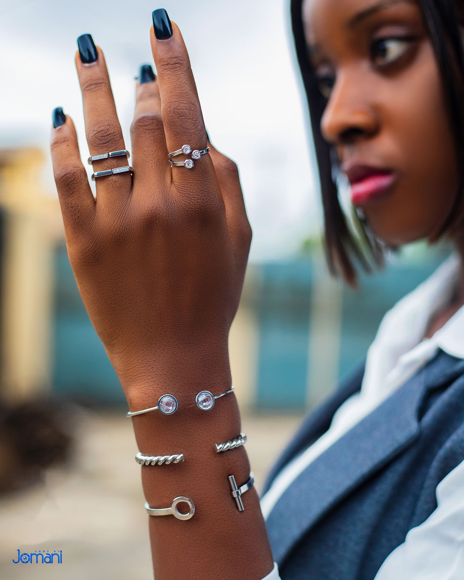 Woman displaying silver bracelets and rings on her raised hand outdoors.