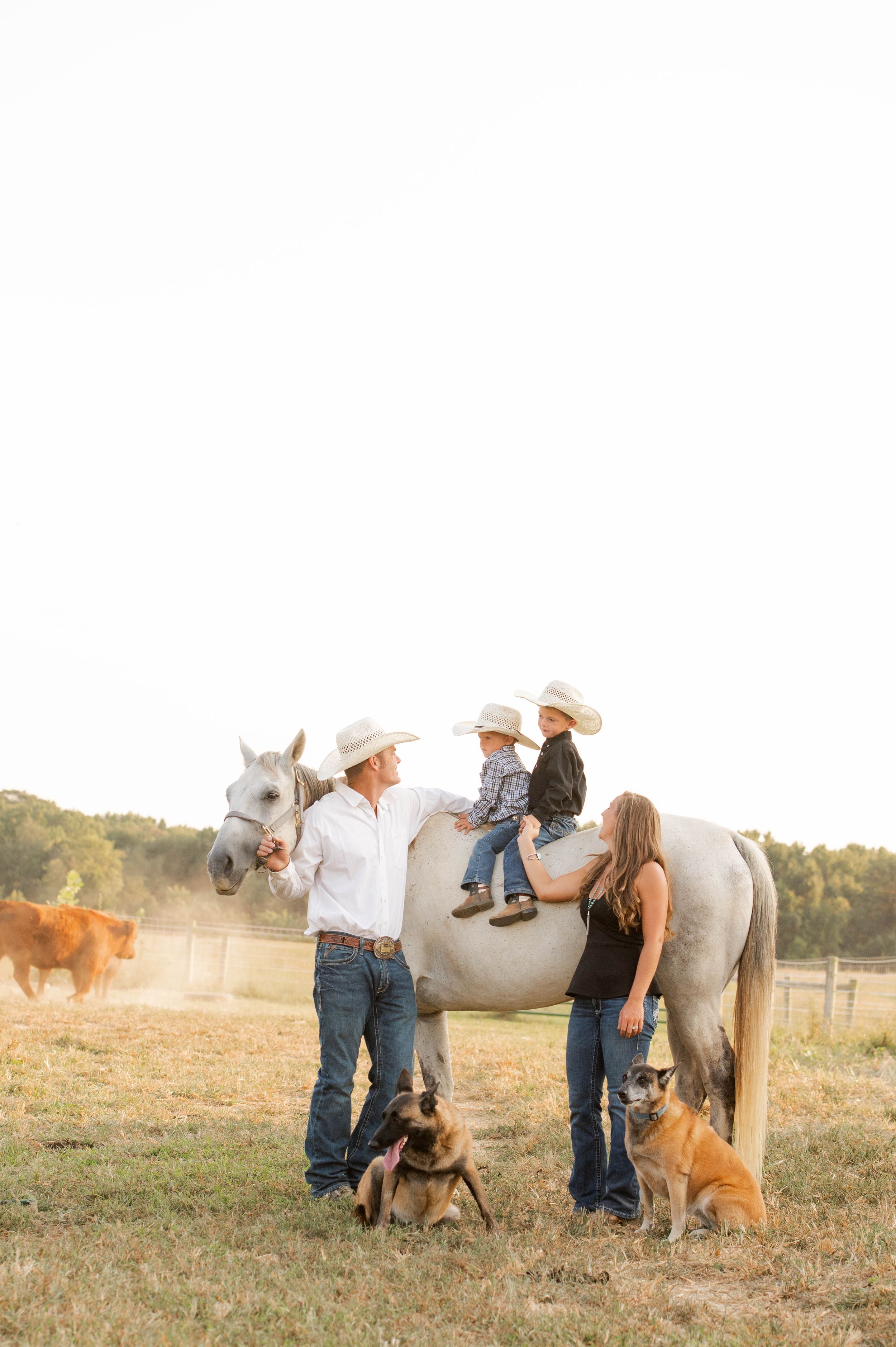 Family with dogs and white horse on rural farm at sunset.