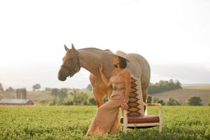 A brown horse stands beside vintage leather boots in a sunny green field.