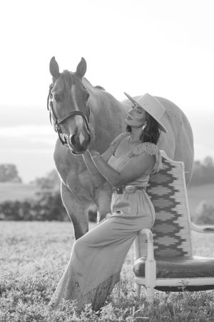 A horse and rider pose next to vintage leather boots in a black and white artistic photo.