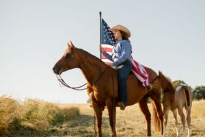 Rider on horseback carries American flag with second horse following in golden field.