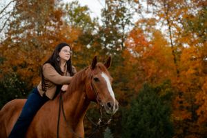 A rider embraces their brown horse surrounded by autumn trees and fall colors.