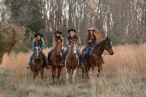 Four riders on horseback pose together in a misty autumn field at sunset.