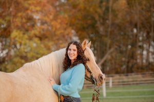 A gentle palomino horse and companion pose together against autumn foliage in a fenced paddock.