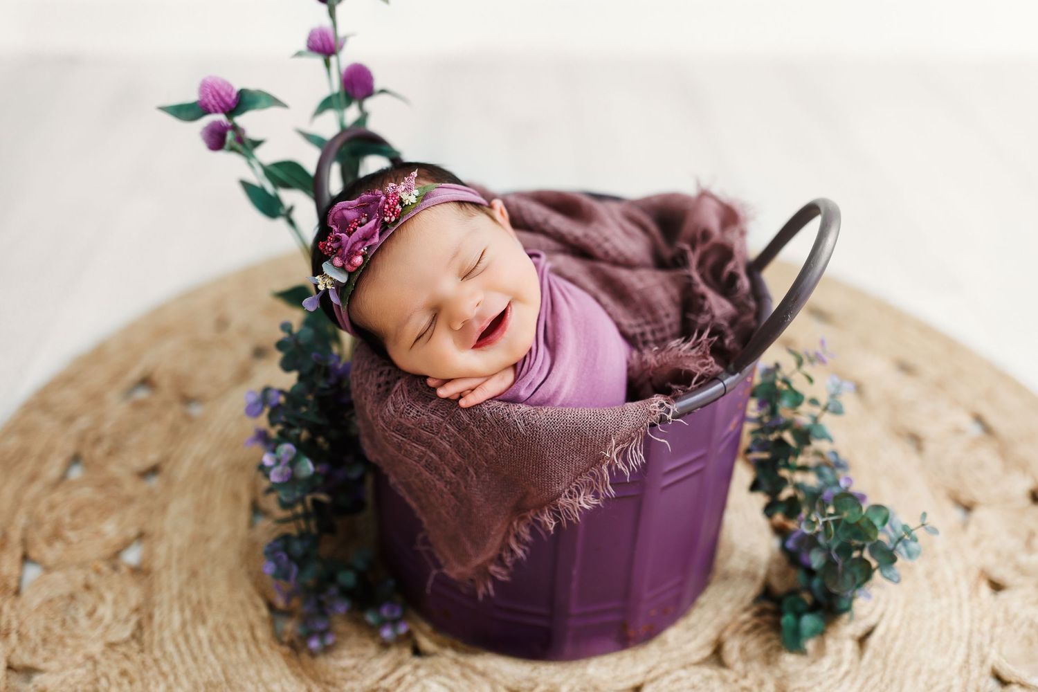 Overhead view of newborn photography setup with scattered purple flower petals and white fabric.