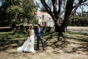 A wedding couple stroll under a large tree in at Rototawai in a sunlit outdoor setting by wedding photographer August and Vine