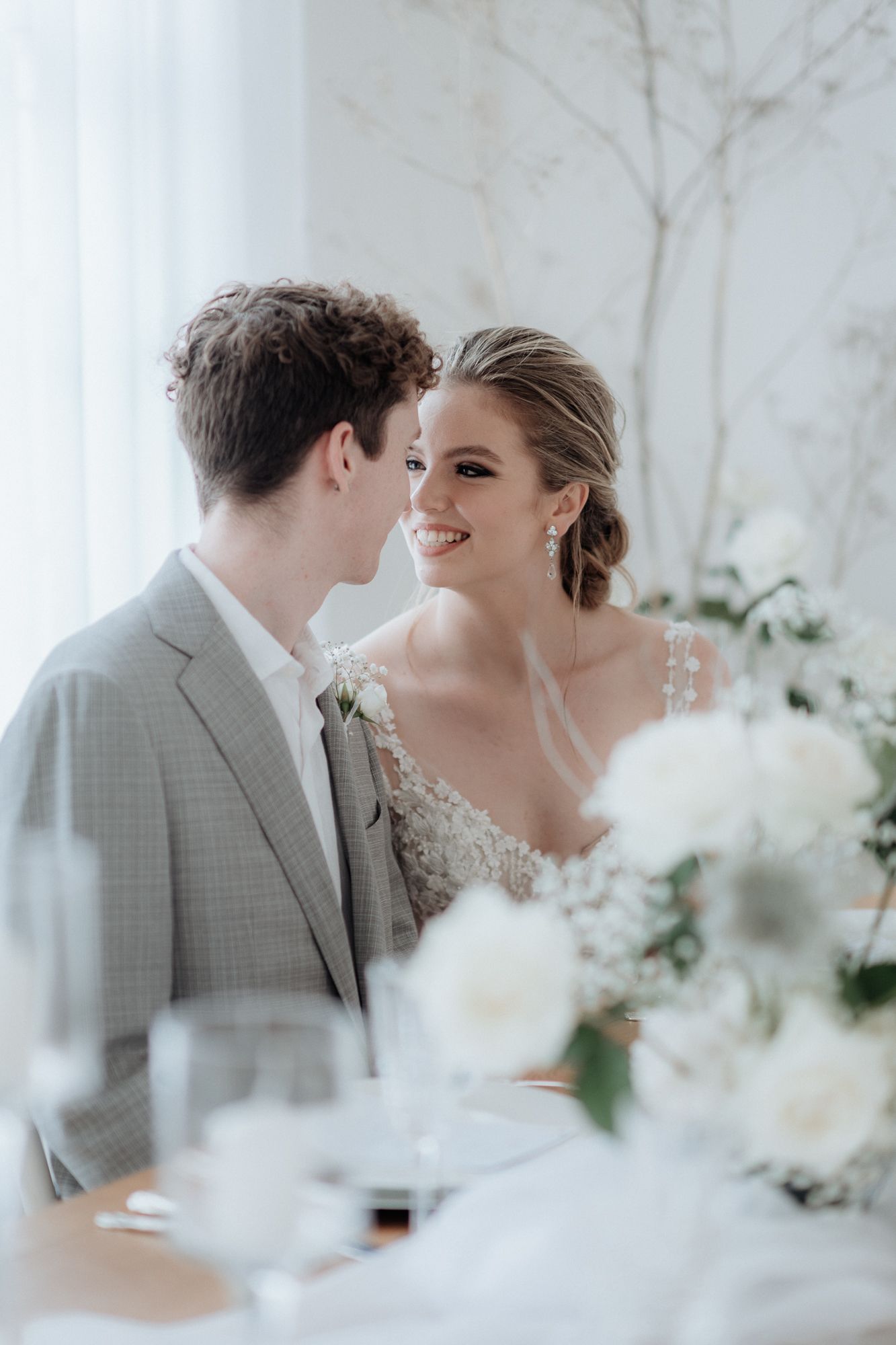 Romantic wedding couple share intimate moment in an elegant white floral setting with soft lighting by wedding photographer August and Vine