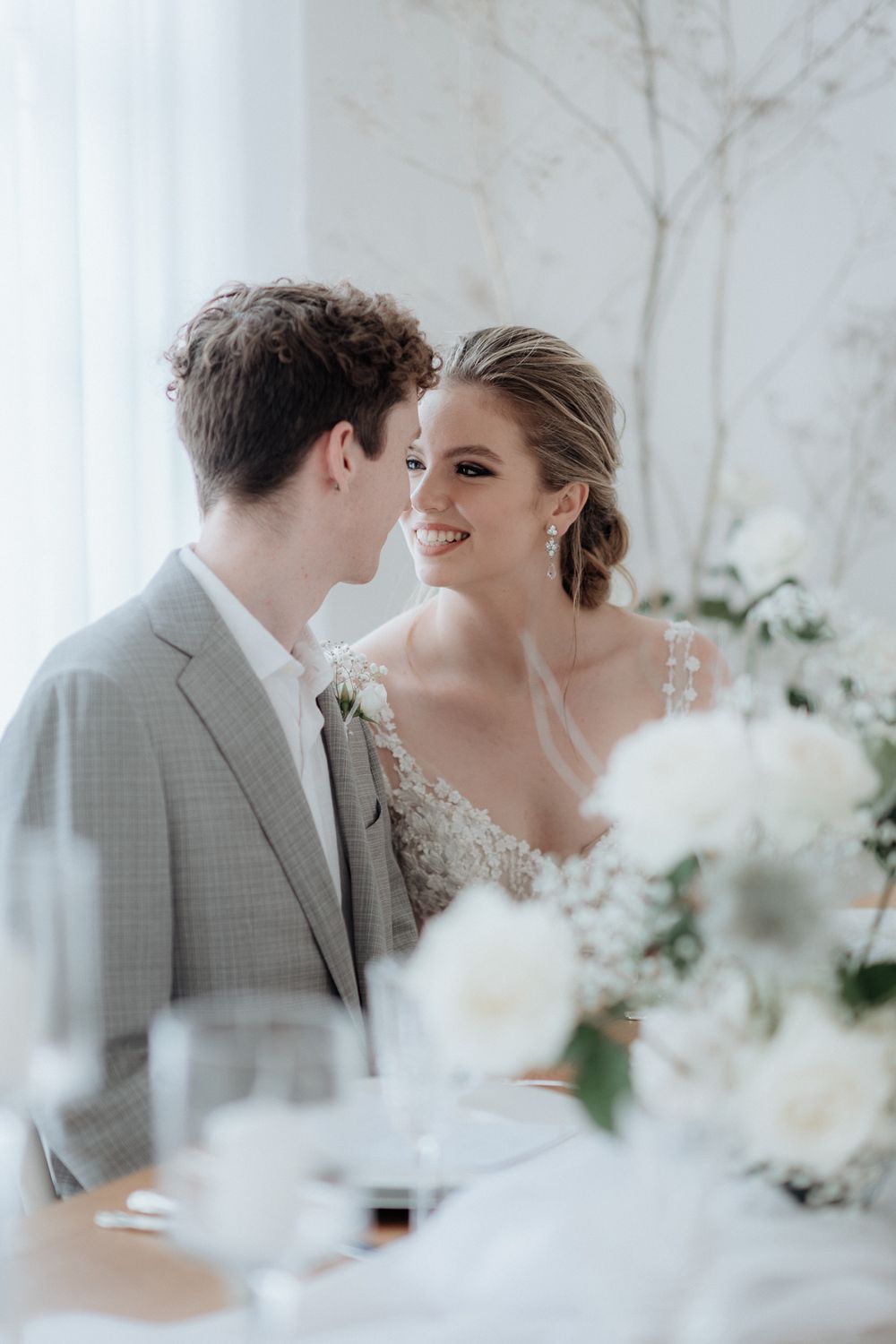 Romantic wedding couple share intimate moment in an elegant white floral setting with soft lighting by wedding photographer August and Vine