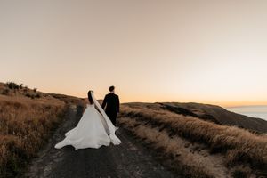 A wedding couple walk along a scenic cliff top at Boomrock Wellington during golden hour sunset by wedding photographer August and Vine.