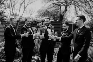 Black and white photo of Groomsmen in formal attire standing outdoors toasting with glasses by wedding photographer August and Vine