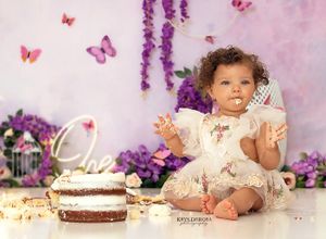 First birthday cake smash photo session with purple flowers, pink butterflies and whimsical decorations.