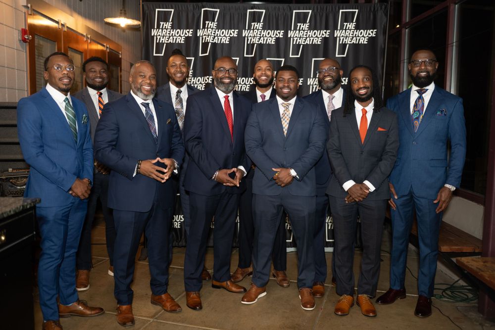 Group of men in formal suits posing together at an evening event.