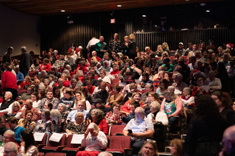 Packed theater audience wearing festive attire during holiday performance.