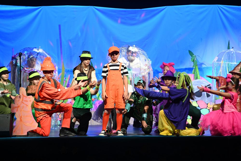Bright theatrical performance featuring actors in colorful costumes against blue backdrop.