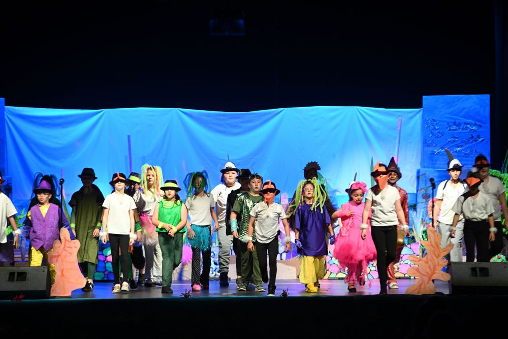 Children's theater performance with colorful backdrop and costumed young actors on stage.