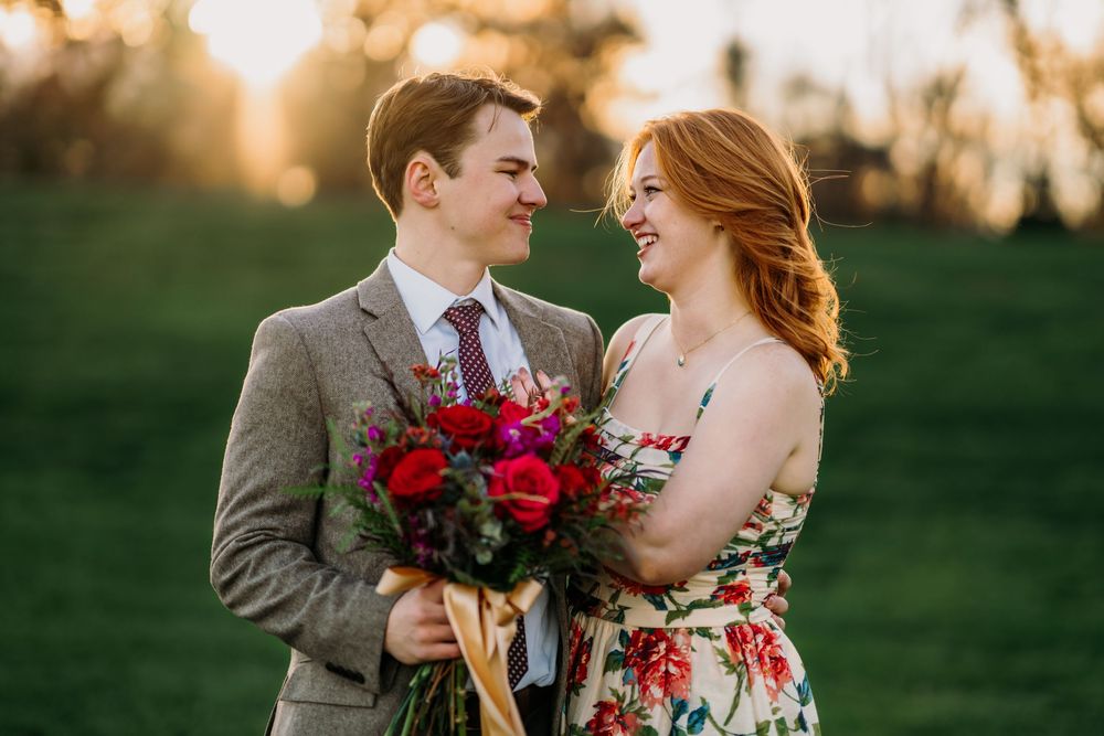 A couple shares a romantic moment outdoors with red floral bouquet at sunset. Couples engagement Photographer Cincinnati proposal