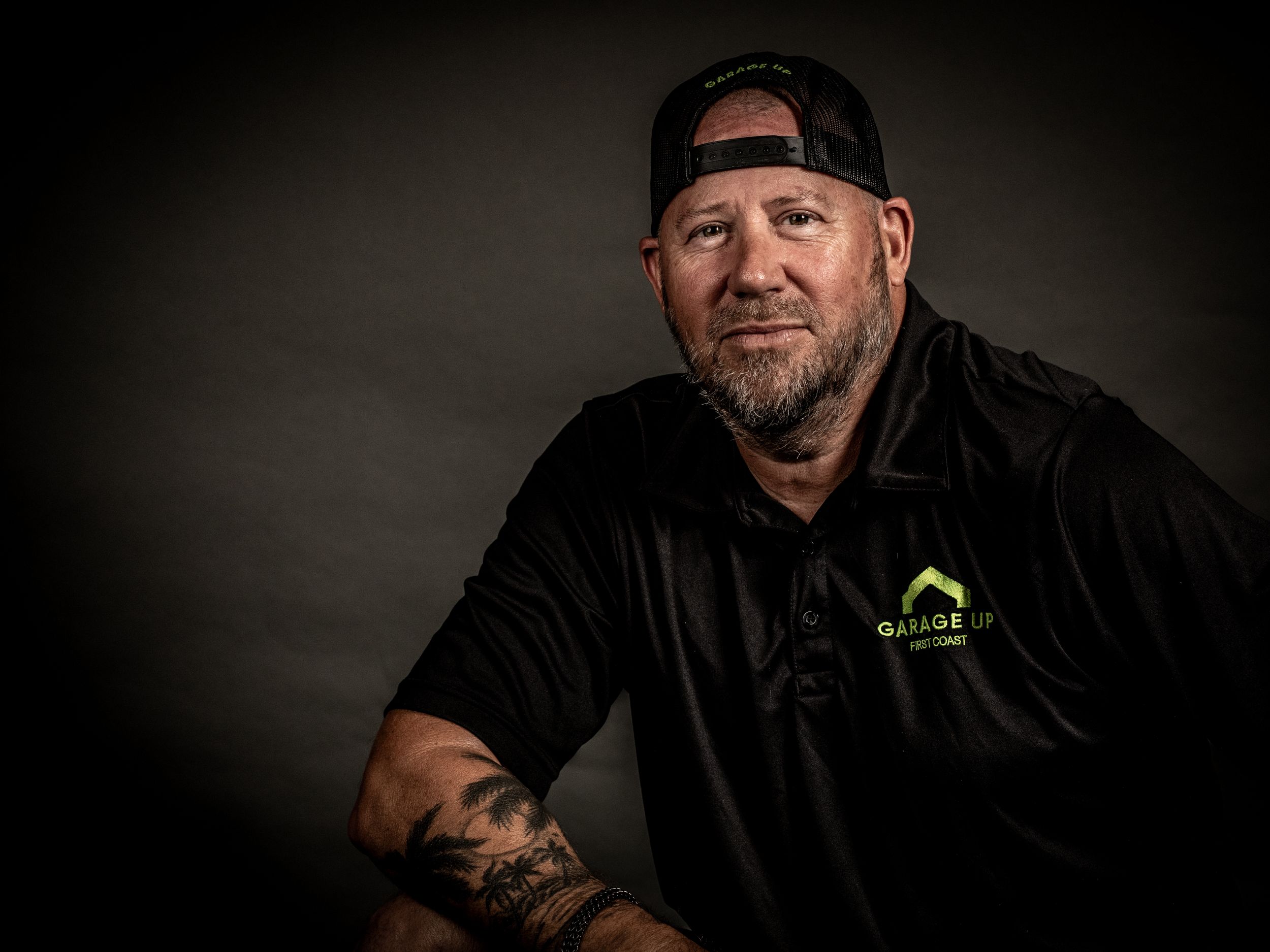 Studio portrait of person wearing black polo shirt and backwards cap against dark background.
