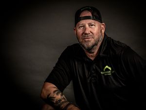 Studio portrait of person wearing black polo shirt and backwards cap against dark background.