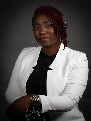 Professional studio portrait featuring a person wearing a crisp white blazer and black top with braided red hair and silver jewelry.