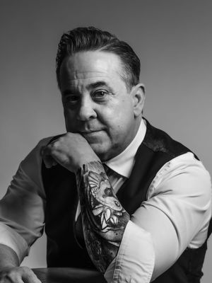 Black and white portrait of a man in formal attire with vest and tie posing thoughtfully with hand near face.